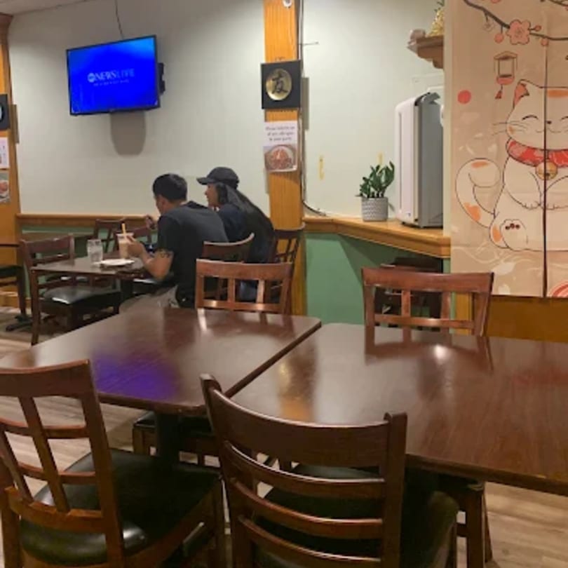 Two patrons dining at a table in Donburiya Cafe, with empty tables and Japanese decor nearby.