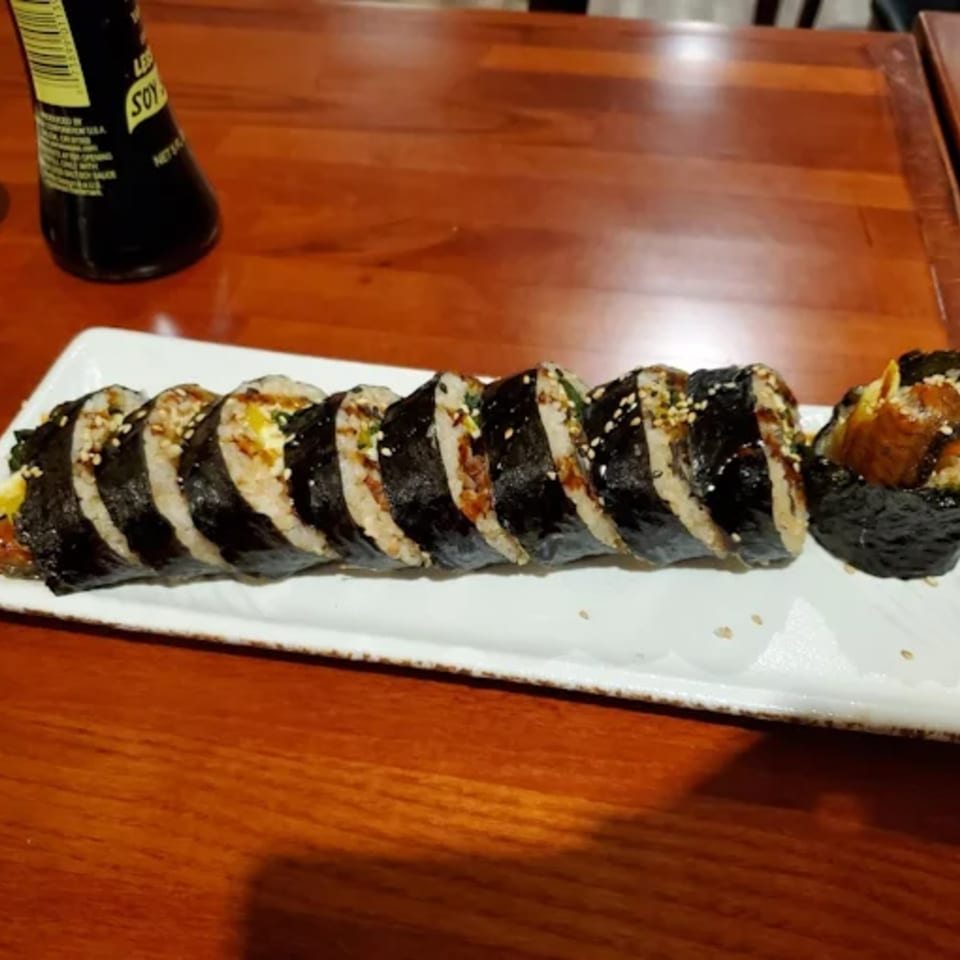A plate of sliced Donburiya Cafe kimbap with sesame seeds on a wooden table.
