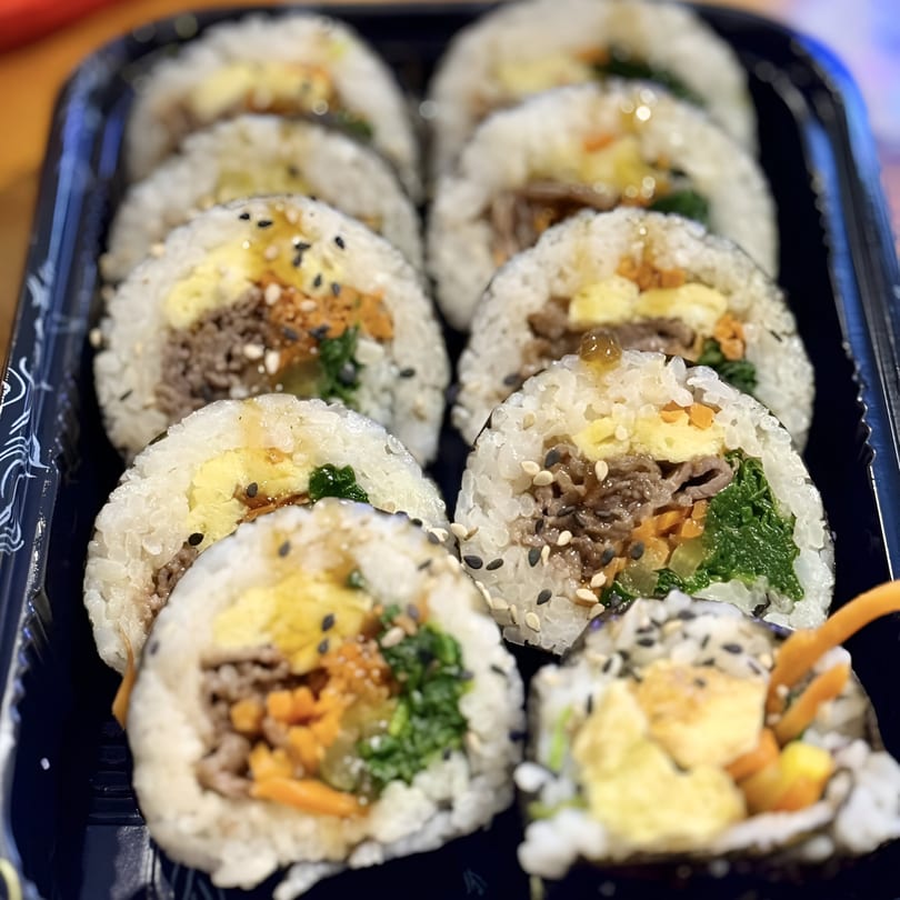 Close-up of Donburiya Cafe's Japanese kimbap rolls with beef, egg, and vegetables in a black tray.